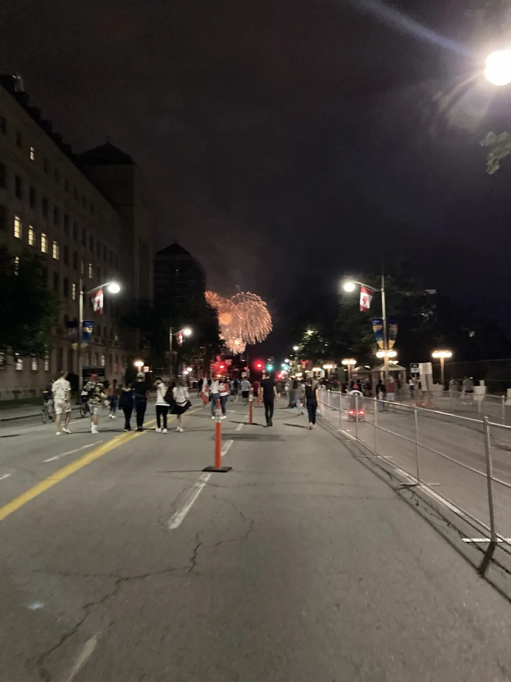 Nighttime street in Ottawa near Parliament with fireworks in the distance and security fencing along the road